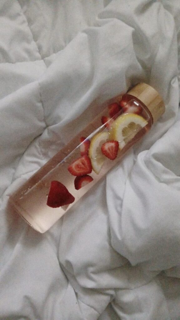 strawberry lemon infused water 🍓 🍋 - Handy Home Glass bottle with sliced strawberries and lemon in water, on a soft white blanket. Refreshing fruit-infused detox drink.