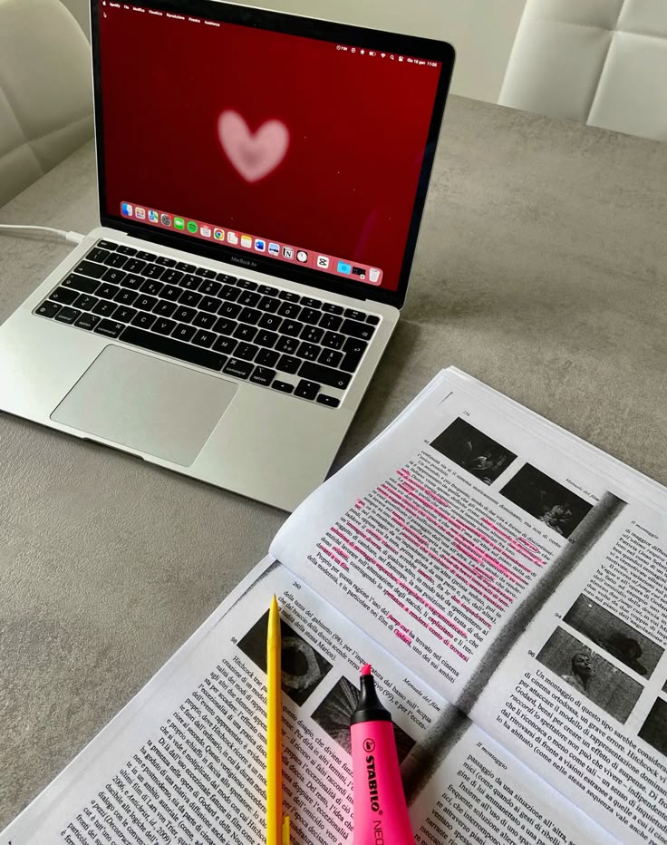 studying - Handy Home Open laptop with a heart wallpaper, next to documents highlighted for study on a desk.