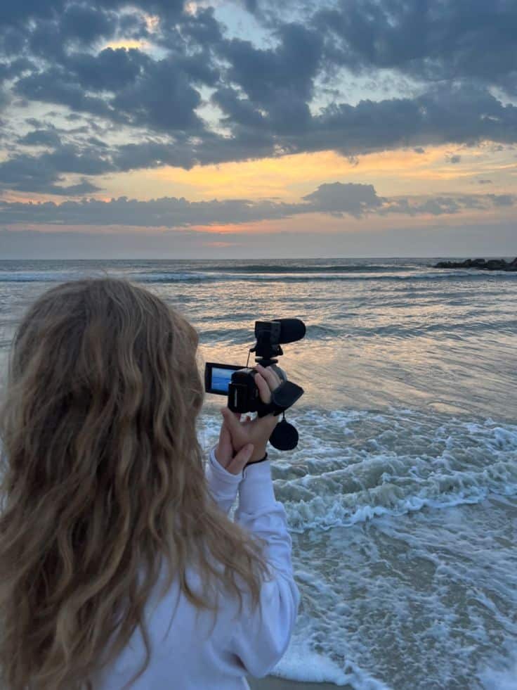 sunrise - Handy Home Person filming a serene ocean sunset with a camcorder, capturing waves and a colorful sky.