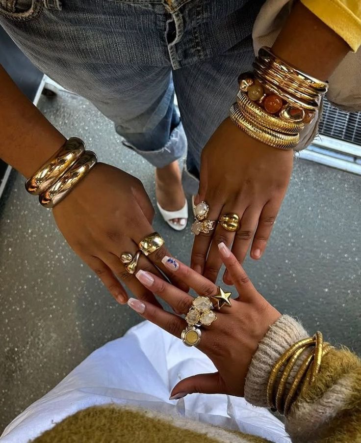 trendy chunky jewelery ⭐️ - Handy Home Diverse hands adorned with gold rings and bangles, showcasing trendy jewelry against casual denim and cozy sweater outfits.