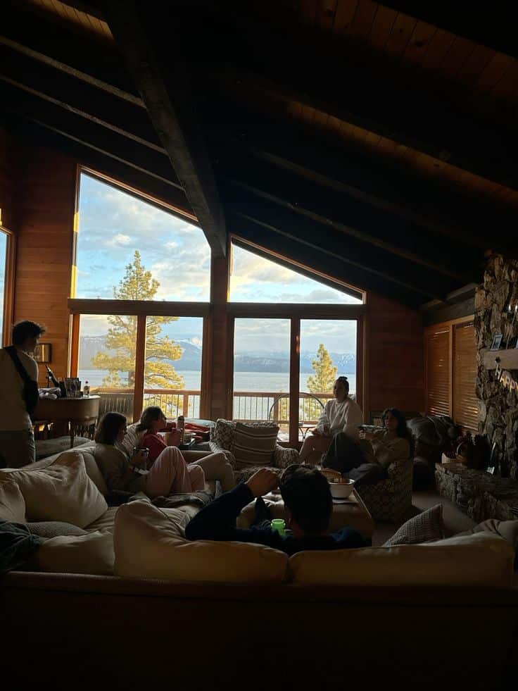 winter cabin trip _ Lake Tahoe Cozy cabin interior with people relaxing on sofas, large windows reveal a scenic lake and mountain view in the background. - Handy Home Cozy cabin interior with people relaxing on sofas, large windows reveal a scenic lake and mountain view in the background.