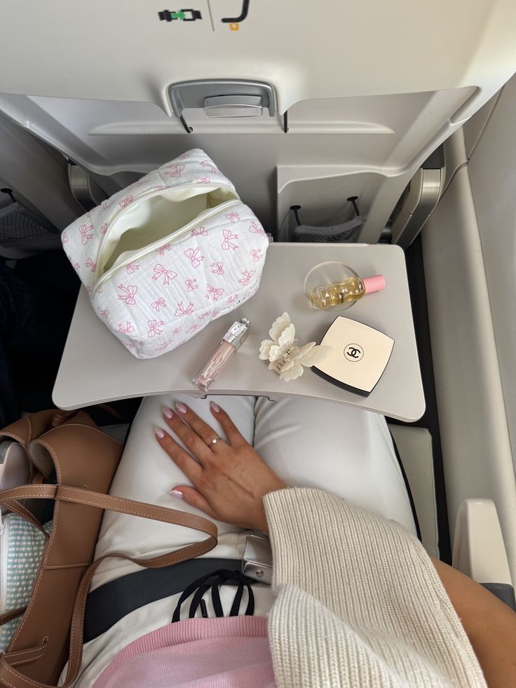✈️🎀🤍 - Handy Home Airplane tray with beauty essentials, perfume, and a travel pouch. Passenger with manicured nails and handbag visible. Travel style.
