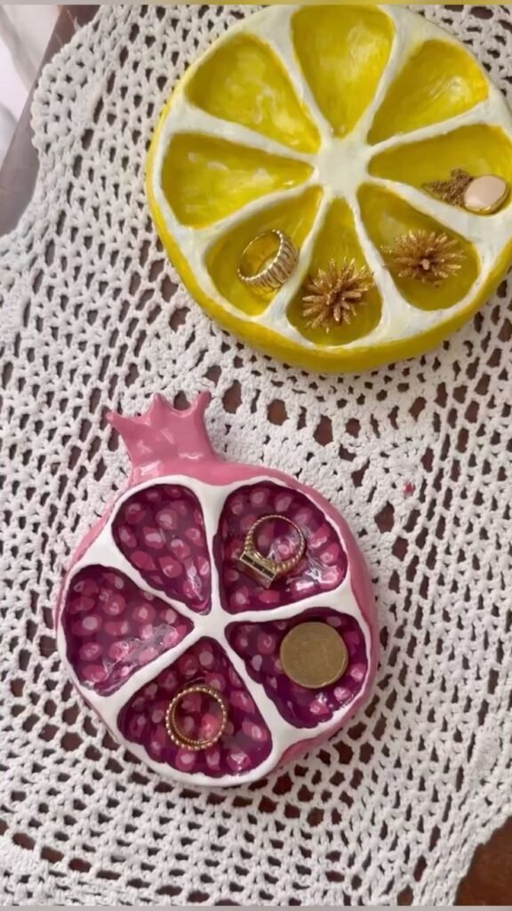 Colorful fruit-shaped jewelry trays with rings and coins on a crochet doily.