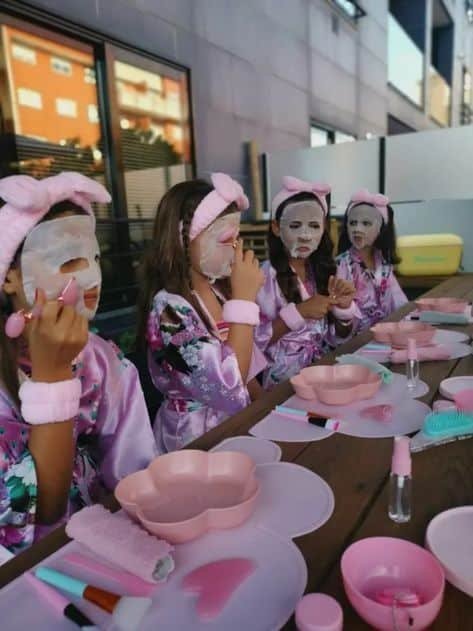 22+ Teenager Sleepover Party Ideas For An Unforgettable Night - MOMtivational Kids enjoying a spa-themed party with face masks and robes, seated at a table with beauty supplies and pink accessories. - Handy Home Kids enjoying a spa-themed party with face masks and robes, seated at a table with beauty supplies and pink accessories.