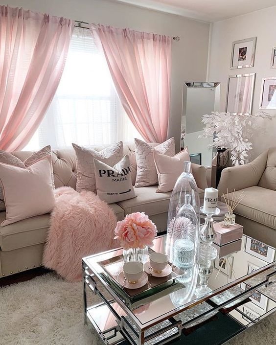 Chic living room with pink accents, comfy sofa, plush pillows, and a mirrored coffee table styled with elegant decor.