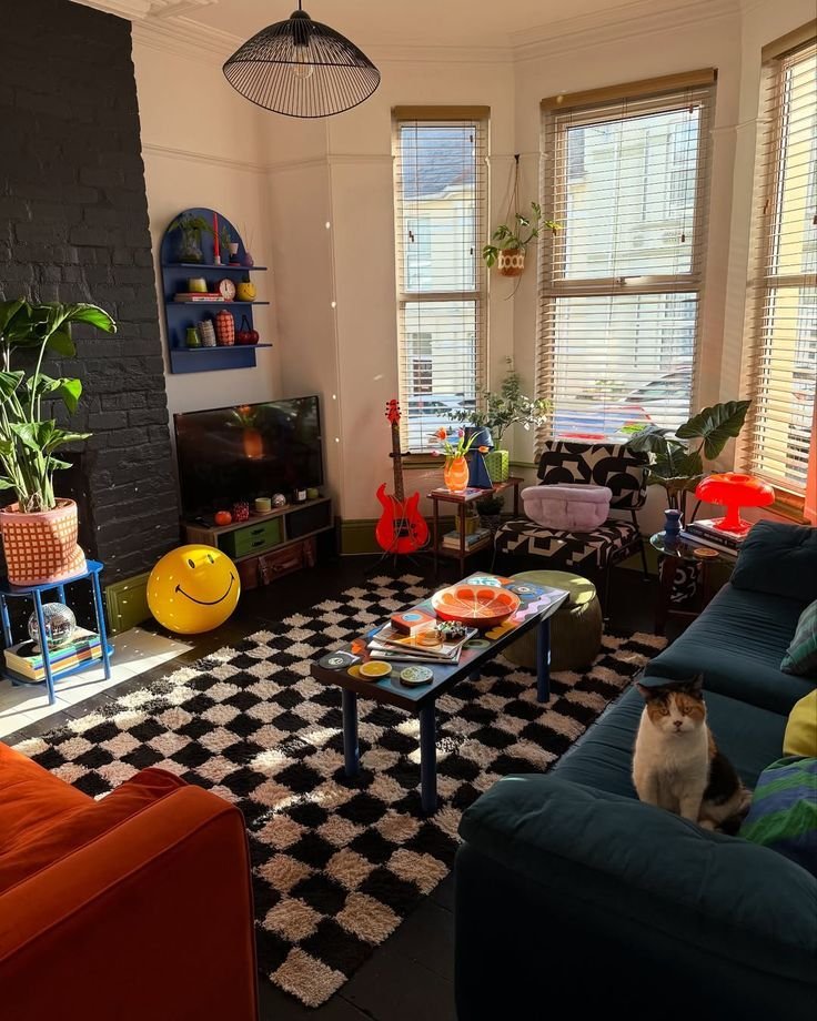 Vibrant living room with eclectic decor, checkered rug, colorful accents, and a cat on the sofa. Cozy, artistic space.