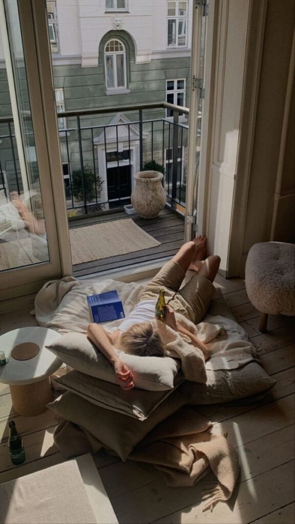 27b810de-ff3c-4bd7-8a47-b03b5366ba34 Person relaxes indoors with a book and a drink, basking in sunlight by open balcony doors with a city view. Cozy home leisure scene. - Handy Home Person relaxes indoors with a book and a drink, basking in sunlight by open balcony doors with a city view. Cozy home leisure scene.