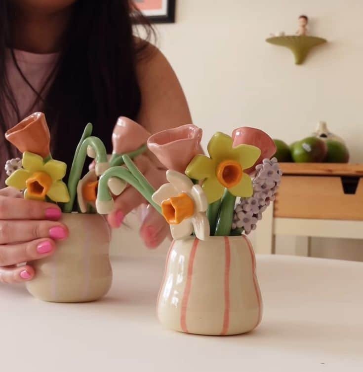 Colorful ceramic flower vases with daffodils and calla lilies on a table, showcasing handmade pottery craftsmanship.