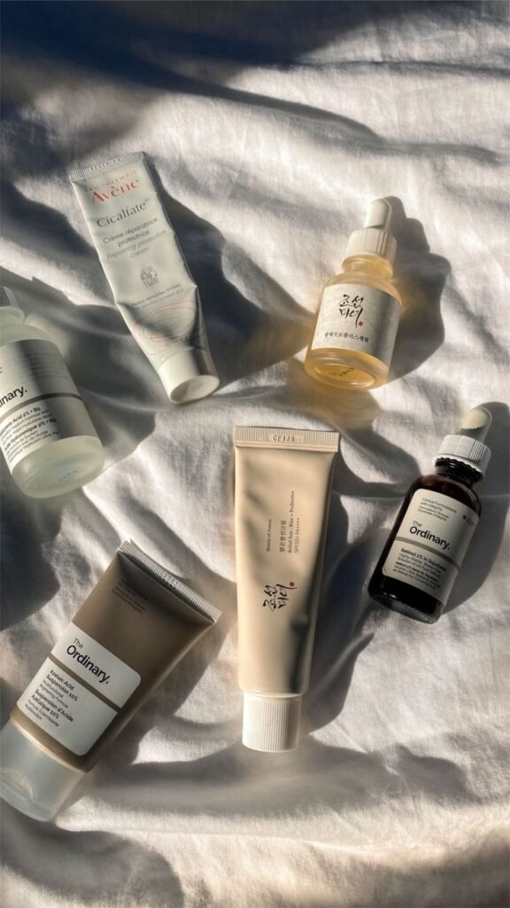 Assorted skincare products on white fabric, featuring serums and creams from popular beauty brands in natural lighting.