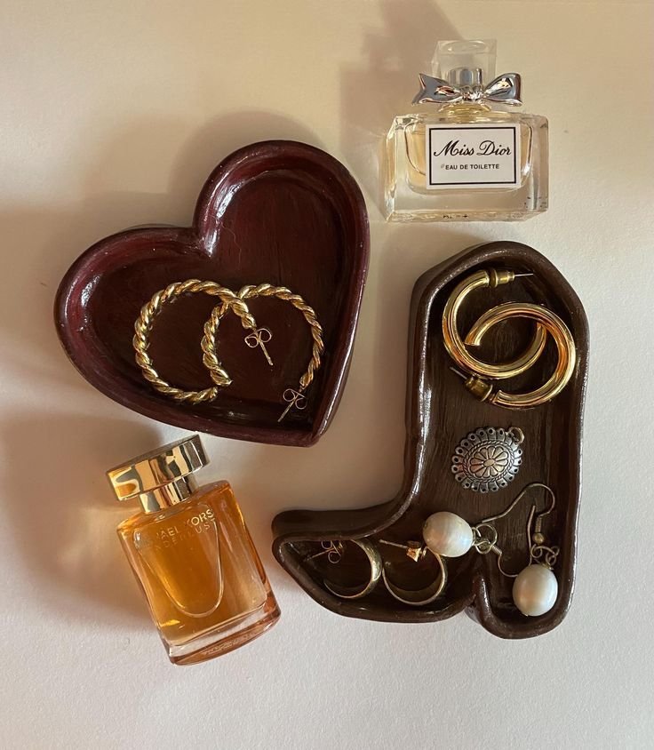 Heart and boot-shaped trays with gold earrings and perfume bottles on a white surface. Elegant jewelry and fragrance display.