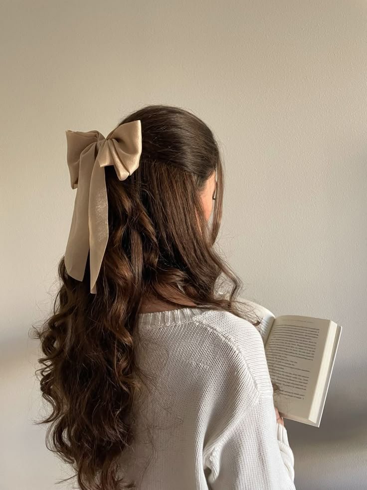 68c02345-7048-4550-b719-4247aa5c4417 Woman with long brown hair and beige bow reads a book while wearing a cozy white sweater. - Handy Home Woman with long brown hair and beige bow reads a book while wearing a cozy white sweater.