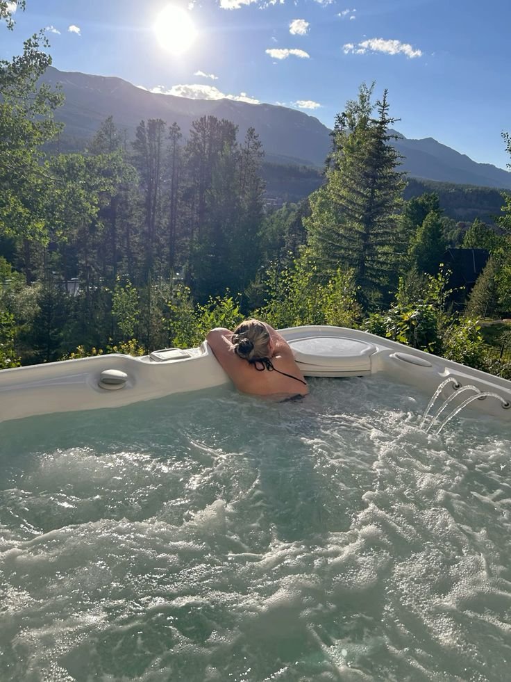Woman relaxing in a hot tub surrounded by lush mountains under a bright sun. Perfect outdoor spa day in nature.