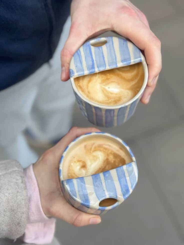 Two hands holding cappuccinos in blue-striped ceramic mugs, showcasing swirling latte art. Perfect for a cozy coffee break.