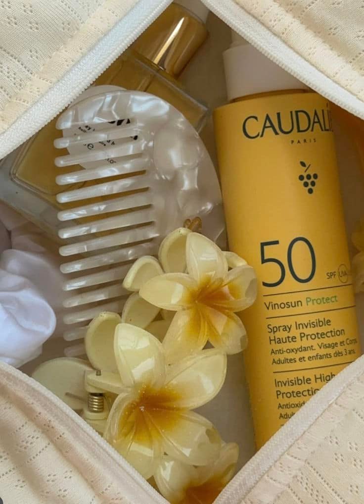 Toiletry bag with SPF 50 sunscreen, comb, perfume, and floral hair accessory. Perfect for summer skincare and hair care essentials.
