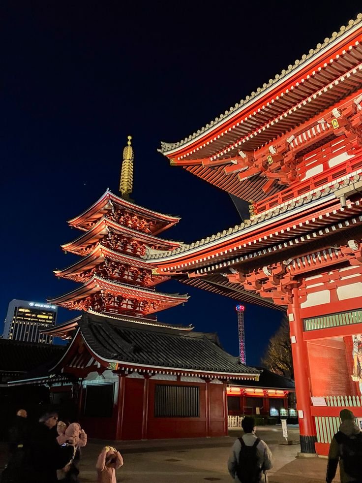 Night view of illuminated Senso-ji Temple, Tokyo, showcasing traditional Japanese architecture and vibrant red pagoda against a deep blue sky.