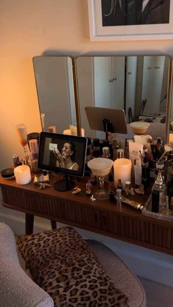 Chic makeup vanity setup with mirrors, skincare products, candles, and iPad tutorial. Cozy leopard print chair adds a stylish touch.