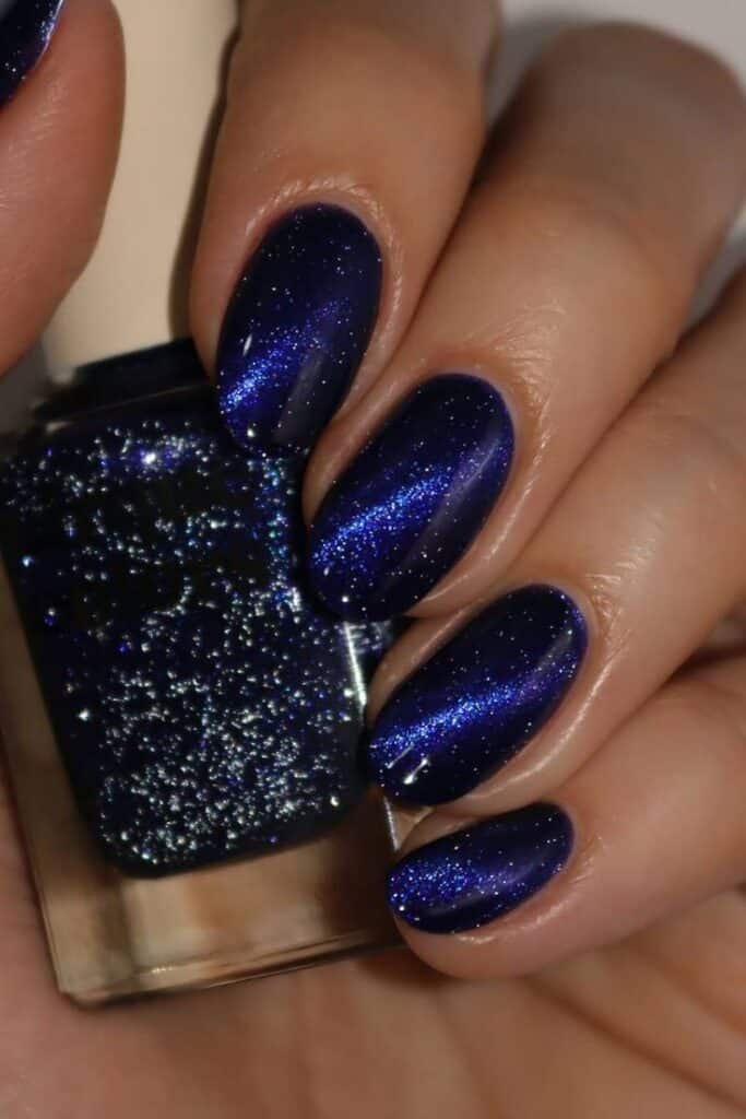 Camera Ready Glittery midnight blue nail polish on manicured nails, showcasing a sparkling and elegant look for evening glamour. - Handy Home Glittery midnight blue nail polish on manicured nails, showcasing a sparkling and elegant look for evening glamour.