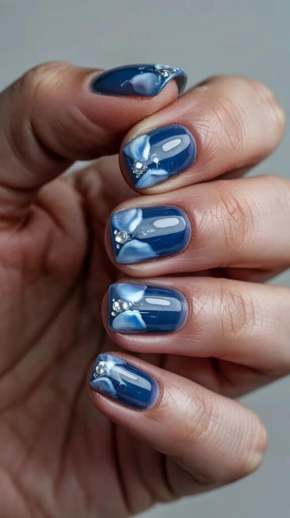 Chic Blue Winter Nails with Frosted Accents Blue nail art with floral accents and rhinestones on manicured nails. Elegant and trendy nail design for a stylish look. - Handy Home Blue nail art with floral accents and rhinestones on manicured nails. Elegant and trendy nail design for a stylish look.