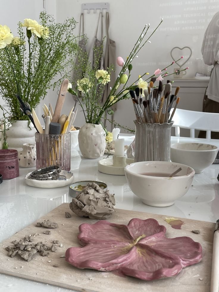 Art studio with clay flower sculpture, brushes, and vibrant flowers, creating a serene and creative workspace.