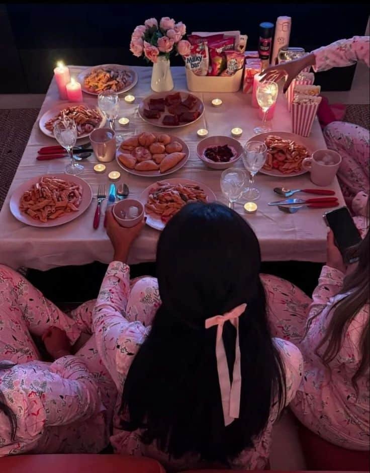 Cutesy Cozy pajama party with food, candles, and friends gathered around a table. Festive snacks, pasta, and flowers add charm. - Handy Home Cozy pajama party with food, candles, and friends gathered around a table. Festive snacks, pasta, and flowers add charm.