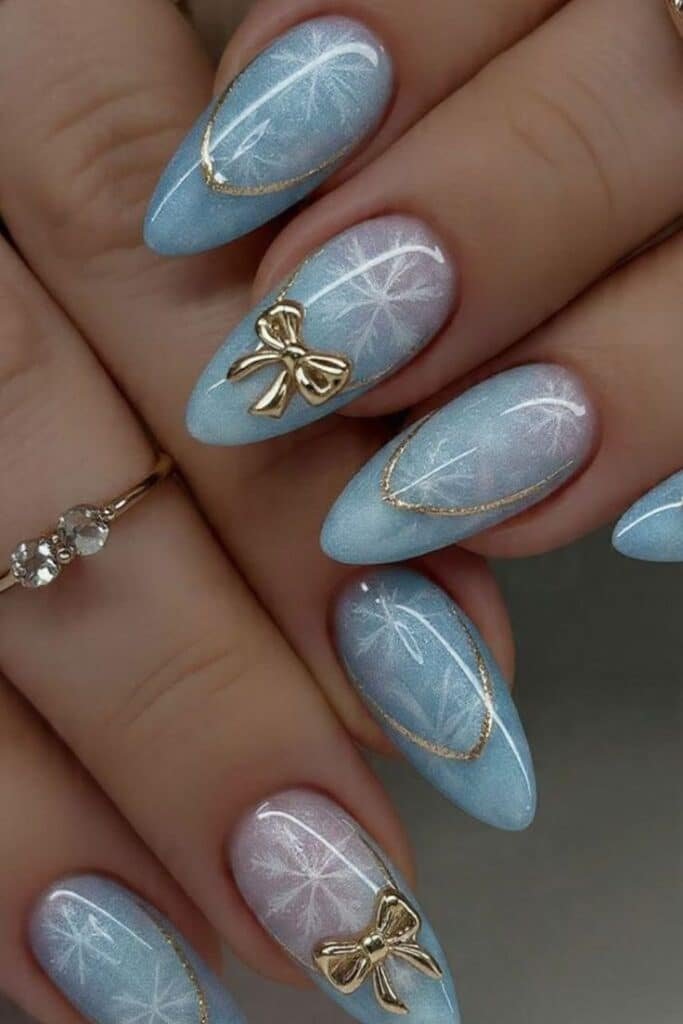 Elegant Icy Blue Winter Nails with Gold Bow Details ❄️💎 Elegant blue ombre winter nail design with gold bow accents and snowflake patterns on long almond-shaped nails. - Handy Home Elegant blue ombre winter nail design with gold bow accents and snowflake patterns on long almond-shaped nails.