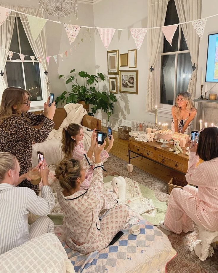 Girls in pajamas capturing a birthday celebration with a cake in a cozy, decorated room.