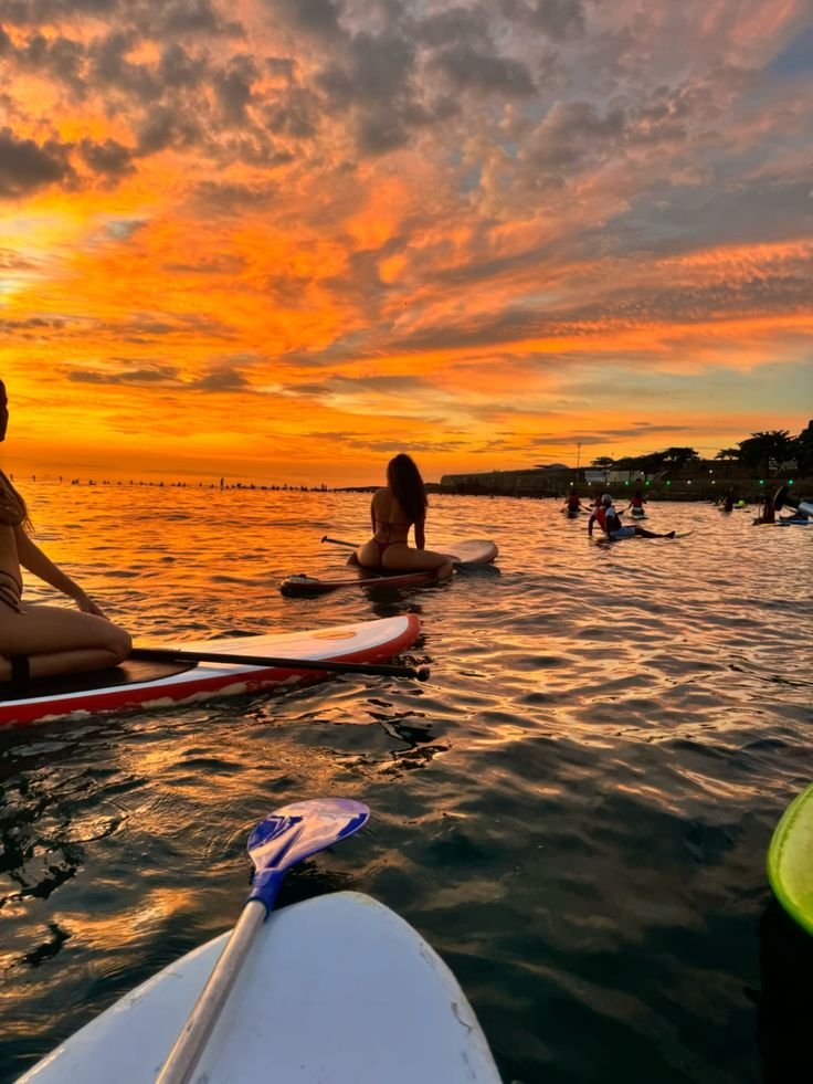 People paddleboarding at sunset with vibrant orange skies and calm water reflections. Stunning evening water adventure.