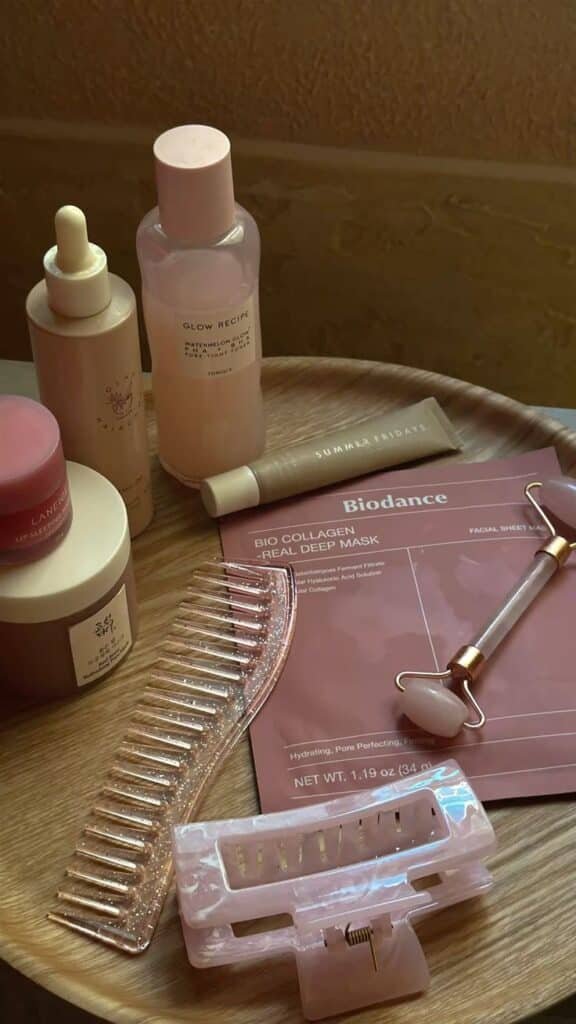 Skincare essentials on a wooden table: serums, masks, roller, and hair accessories for a relaxing beauty routine.