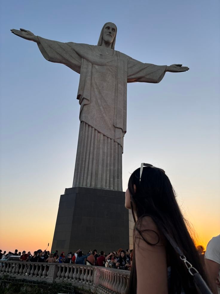 Woman admiring Christ the Redeemer statue in Rio de Janeiro at sunset, surrounded by tourists.