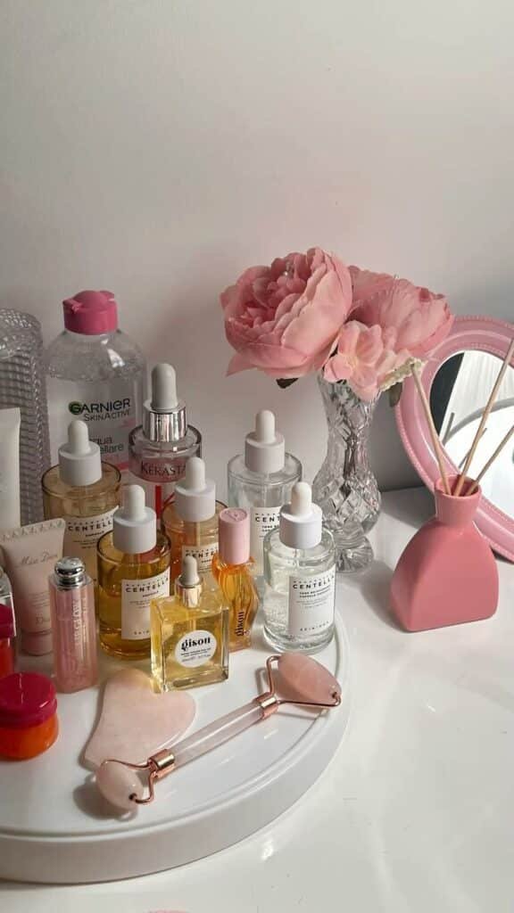 Beauty essentials on a vanity table with skincare products, pink flowers, and a jade roller for a stylish skincare routine setup.