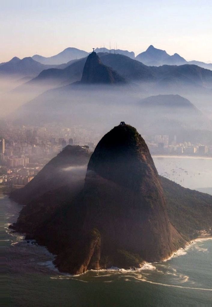 Aerial view of Sugarloaf Mountain in Rio de Janeiro, shrouded in mist, with ocean and cityscape in background.