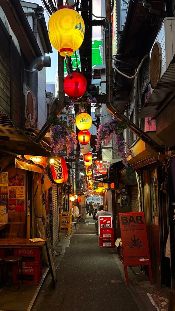 Narrow alleyway in Tokyo adorned with colorful lanterns and signs, bustling with people and vibrant nightlife ambiance.