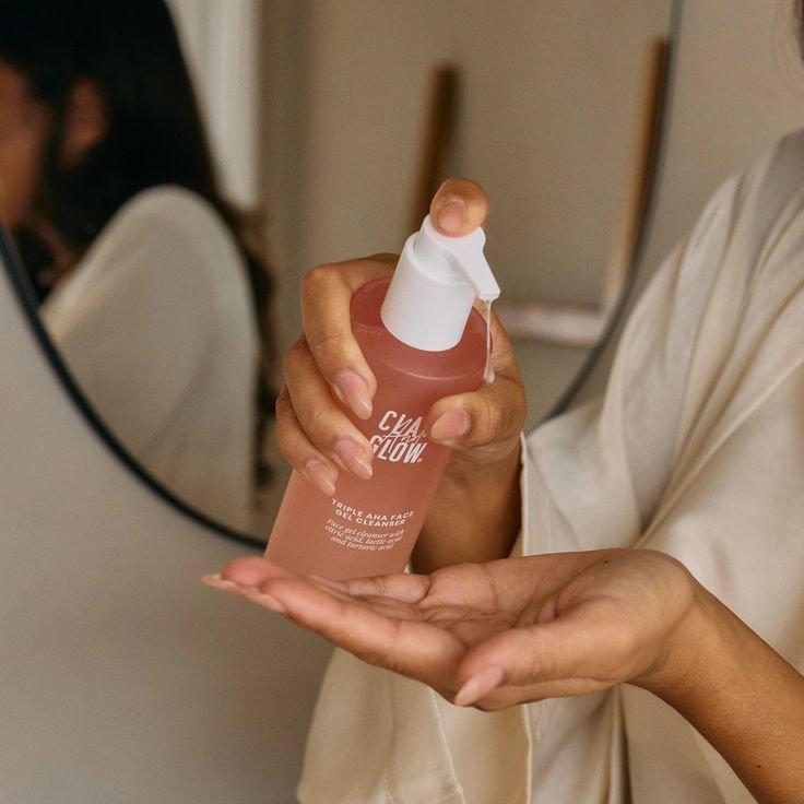 Person dispensing pink skincare serum into hand in front of a mirror, promoting beauty and self-care routine.