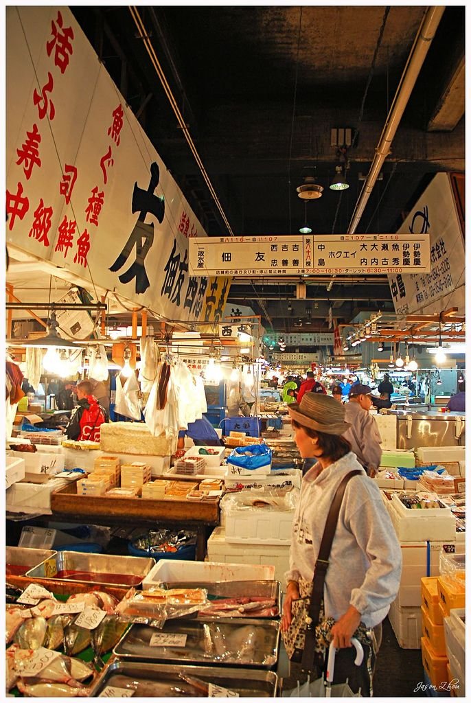 Bustling seafood market with various fresh fish and seafood options; a woman shops amid lively stalls and vibrant signage.