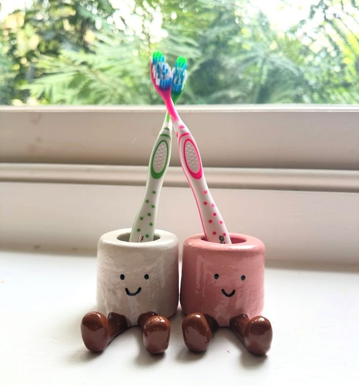 Cute toothbrush holders with smiling faces, each holding a colorful toothbrush, sit on a windowsill with a green garden view.