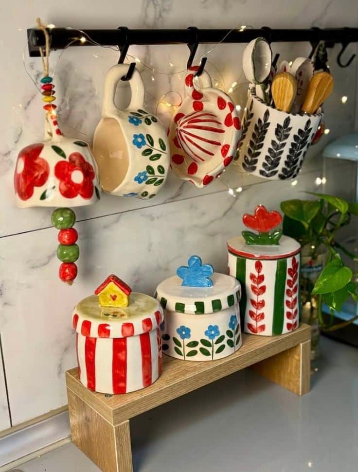 Colorful ceramic mugs and jars with floral patterns on display in a cozy kitchen setting, complemented by decorative lights.