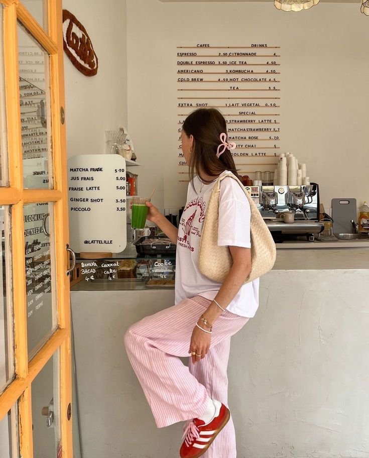 Woman in casual outfit with green juice at a cozy café counter, menu on the wall. Trendy, relaxed vibe.