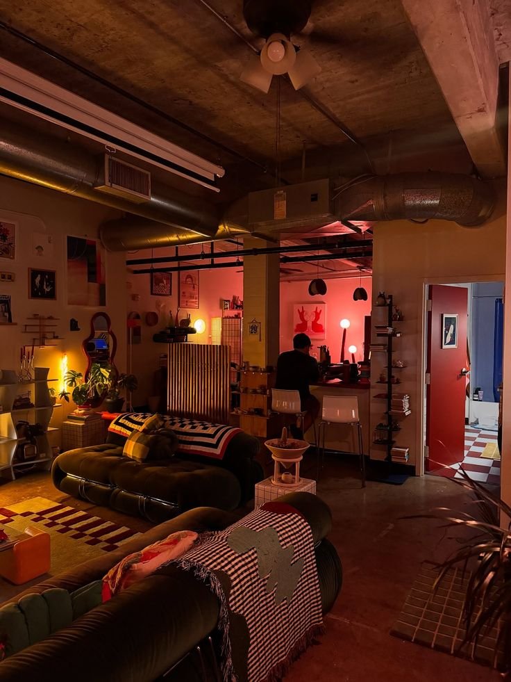 Cozy loft apartment interior with ambient lighting, modern decor, and relaxed seating area. A person sits at the counter in warm tones.