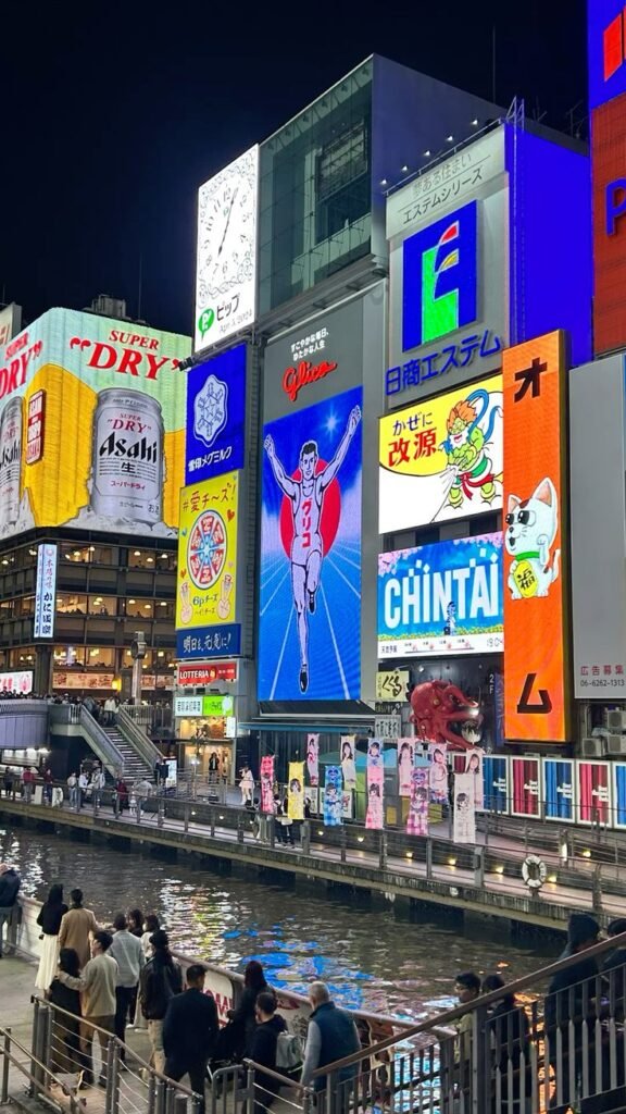 Bright neon signs illuminate Dotonbori, Osaka at night, reflecting vibrantly on the canal water below.