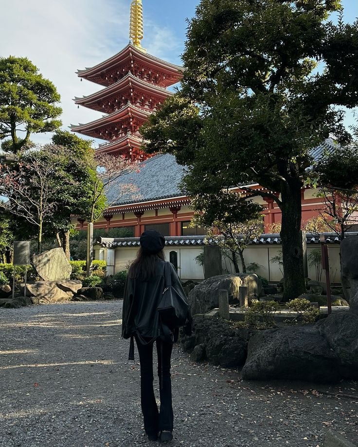 Person walking towards a traditional Japanese pagoda surrounded by lush greenery on a sunny day.