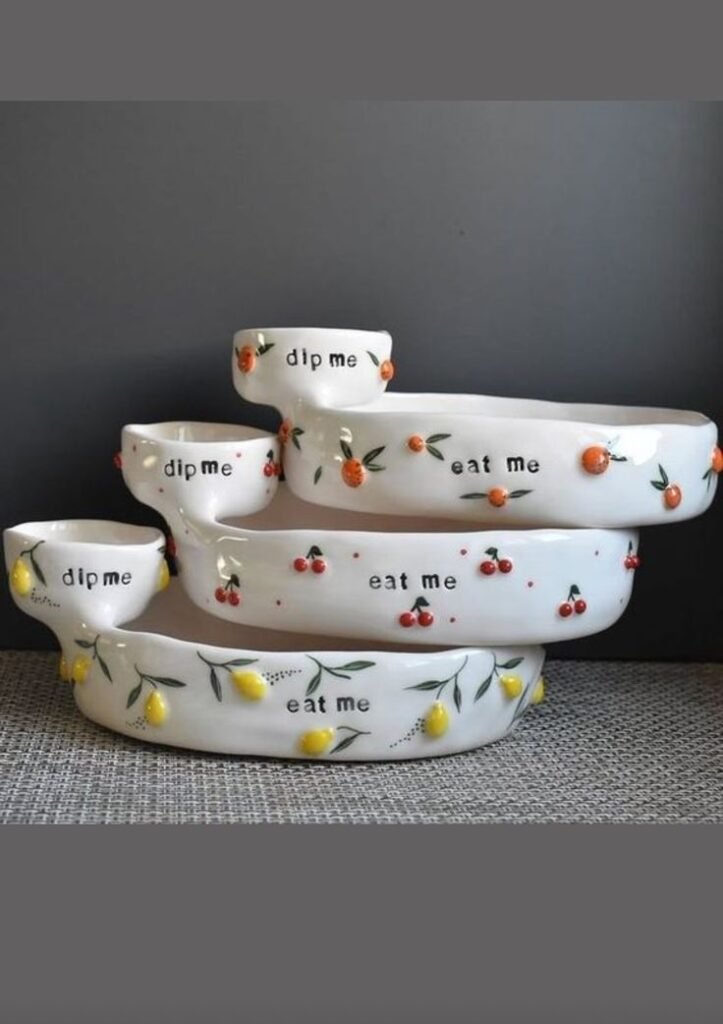 Stacked ceramic bowls with fruit designs and phrases eat me and dip me, ideal for stylish kitchen decor and serving.