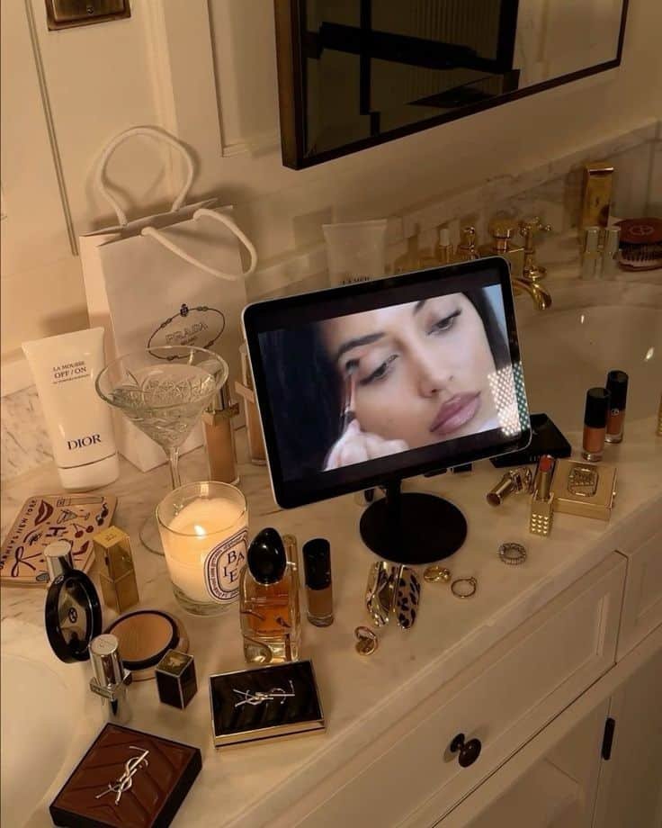 Tablet displaying makeup tutorial amidst luxury cosmetics on a marble vanity with ambient candlelight. Ideal beauty setup.