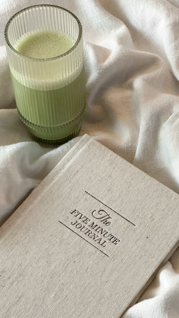 five minutes journal Green matcha latte in a ribbed glass next to The Five Minute Journal on a soft, white fabric. Perfect morning routine setup. - Handy Home Green matcha latte in a ribbed glass next to The Five Minute Journal on a soft, white fabric. Perfect morning routine setup.