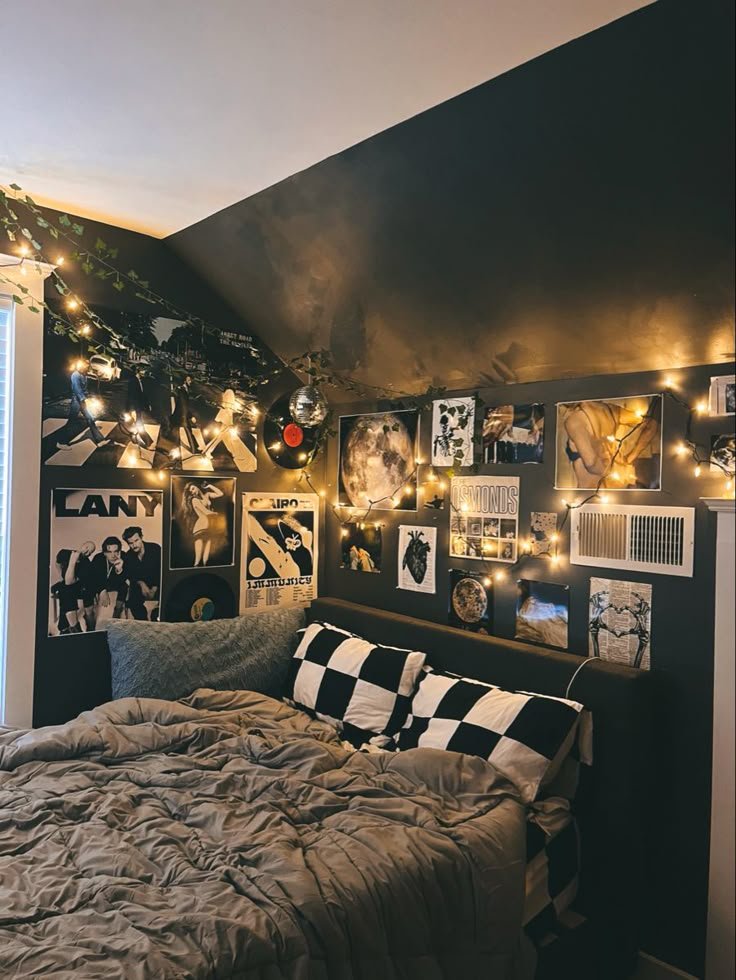Cozy bedroom with dark walls, string lights, and a gallery wall of posters above a bed with checkered pillows. Warm, artistic ambiance.