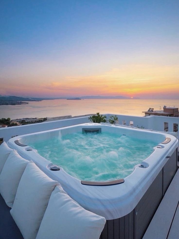 Rooftop jacuzzi with ocean view at sunset, featuring a tranquil sky and plush cushions for ultimate relaxation experience.