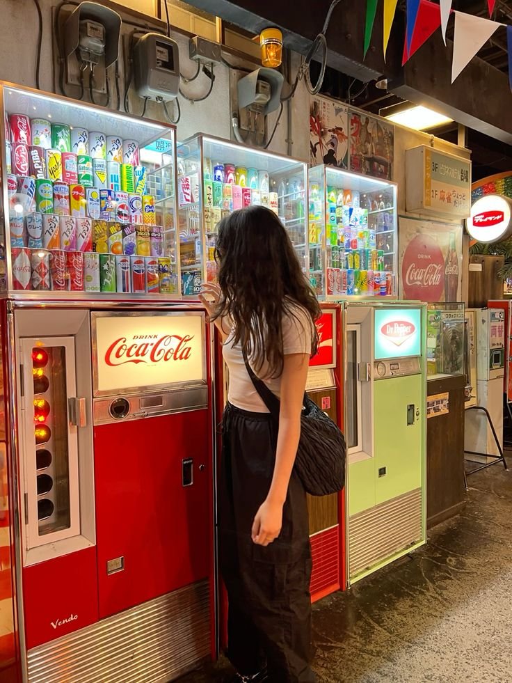 Person selecting drink from vintage Coca-Cola vending machine in retro-themed store, colorful cans on display.