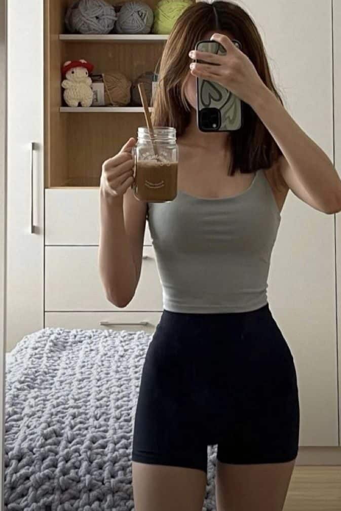 ⏳⏳ Woman taking a mirror selfie, holding an iced coffee in casual outfit, cozy bedroom setting with knitted blanket and yarn shelves. - Handy Home Woman taking a mirror selfie, holding an iced coffee in casual outfit, cozy bedroom setting with knitted blanket and yarn shelves.
