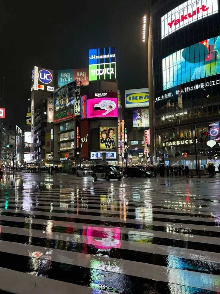 Night view of Shibuya crossing in Tokyo, Japan, with vibrant illuminated billboards reflecting on wet streets.