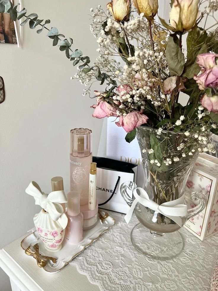 Elegant vanity display with luxury perfumes and dried flowers in a vase, accompanied by designer shopping bags and classic decor.